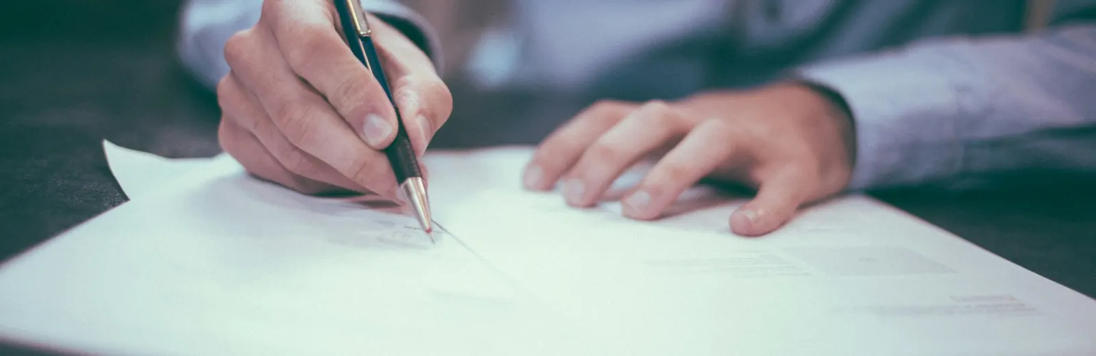 Person filling in a form at a desk with reading glasses beside it